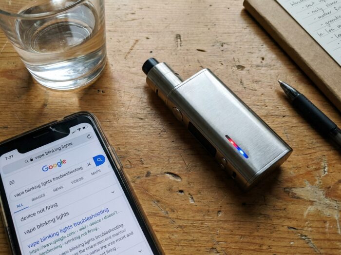 Gros plan sur les voyants LED d'une vapoteuse posée sur un bureau avec smartphone pour dépannage sans notice